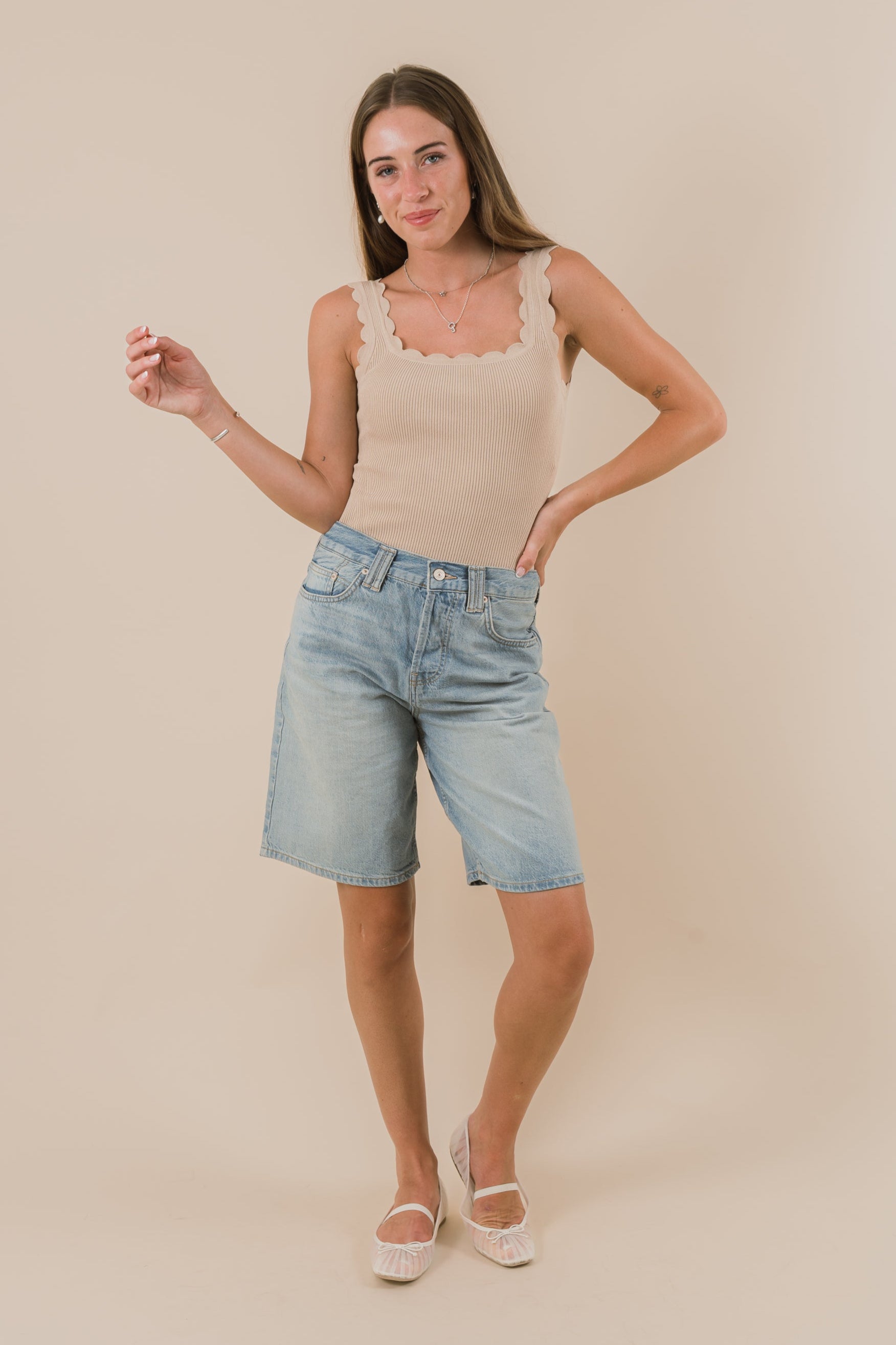 Woman wearing a beige tank top and light blue shorts on a beige background