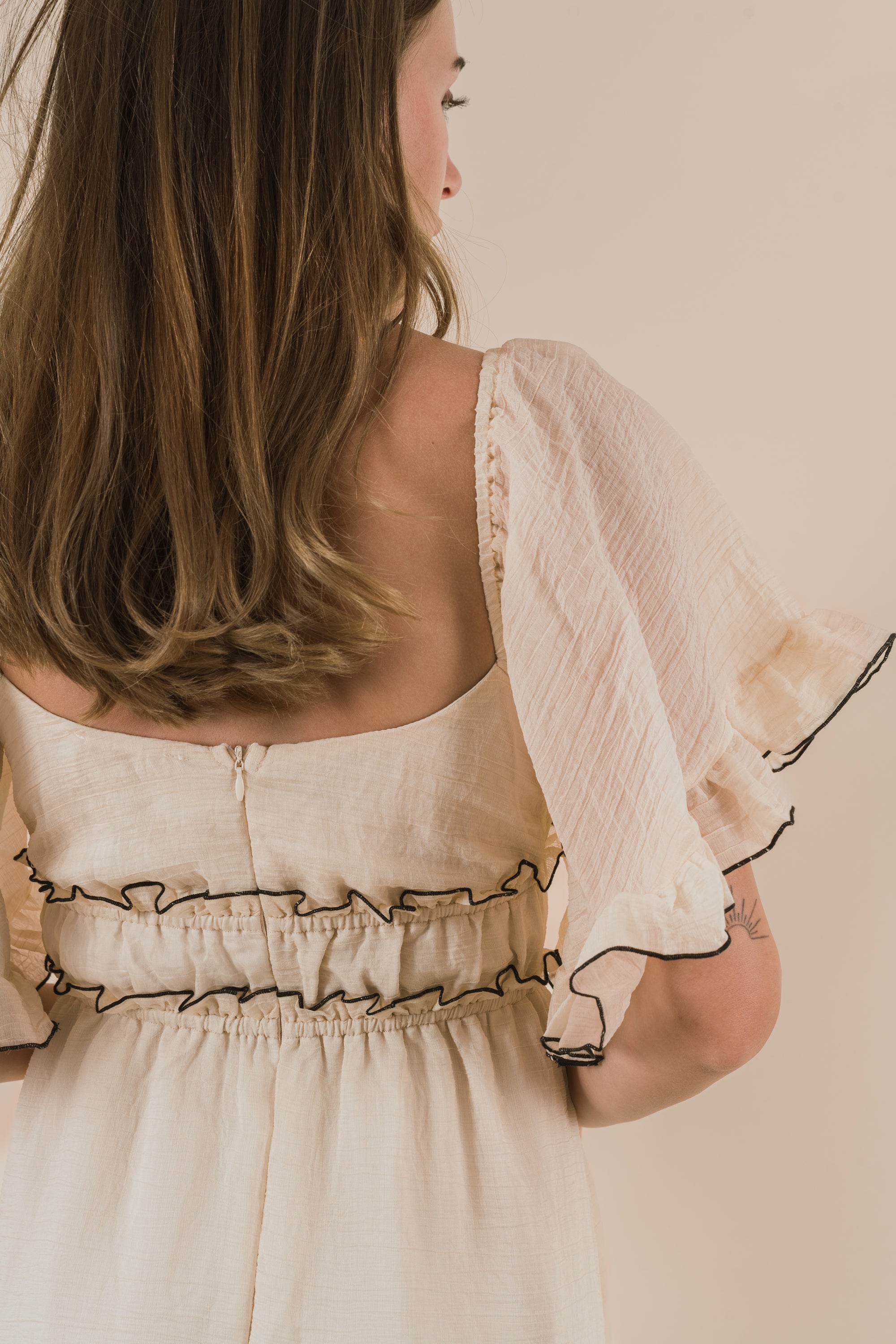 Woman wearing a beige dress with ruffled sleeves against a plain background