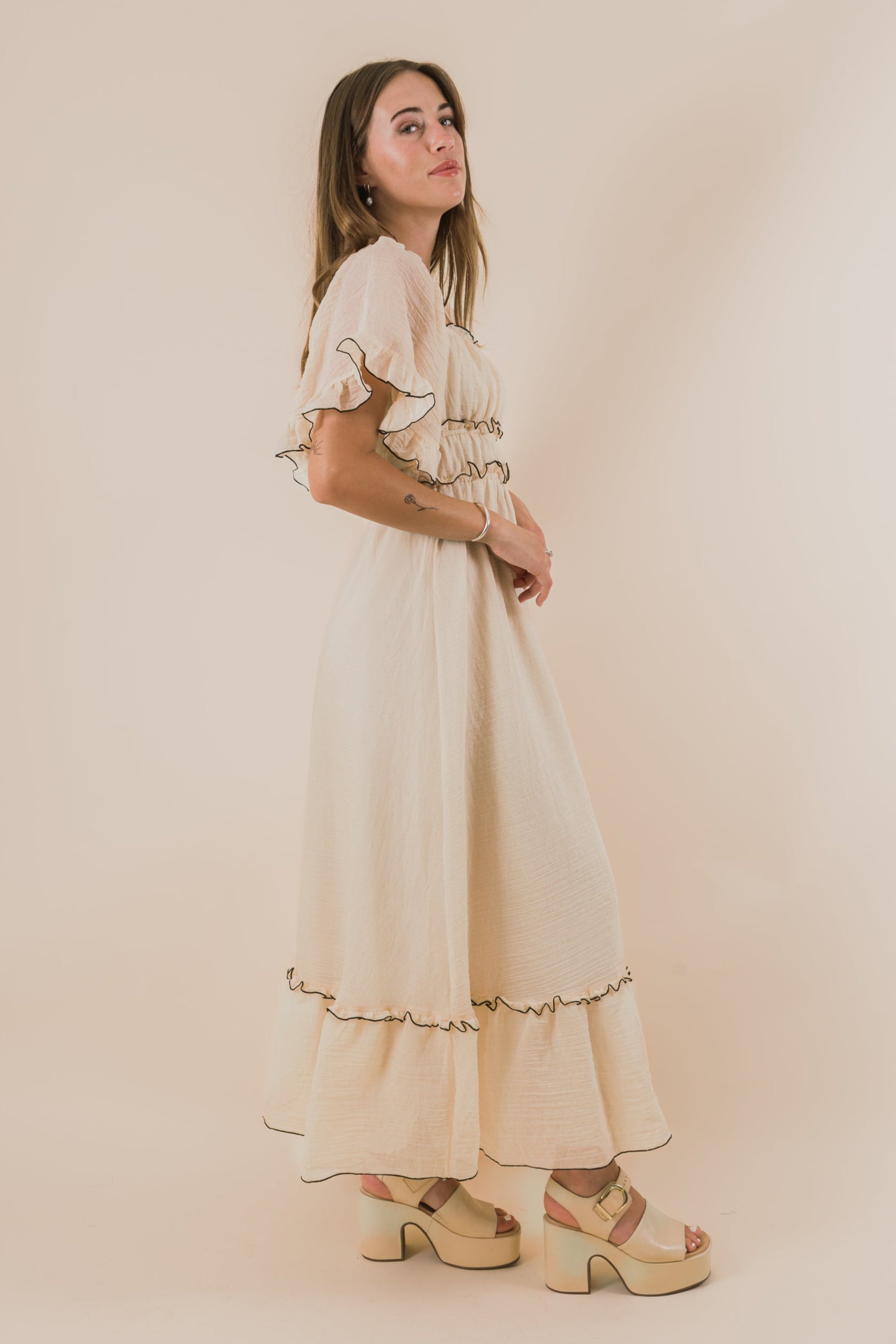 Woman wearing a white dress with ruffled details against a beige background