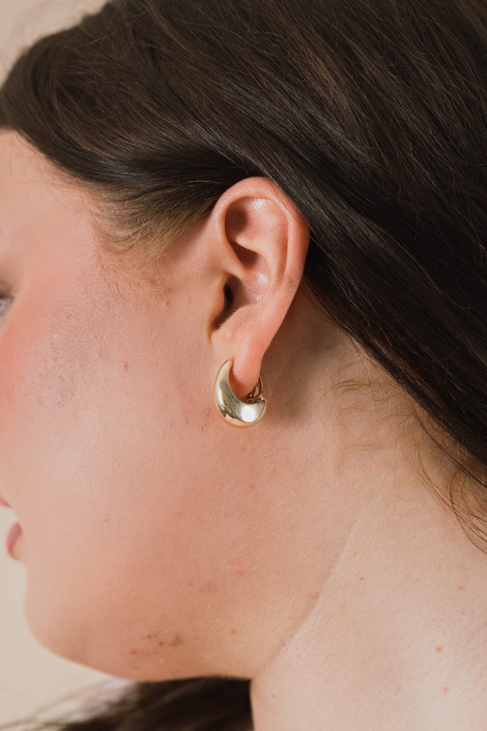 Close-up of a person wearing a gold hoop earring with a neutral background