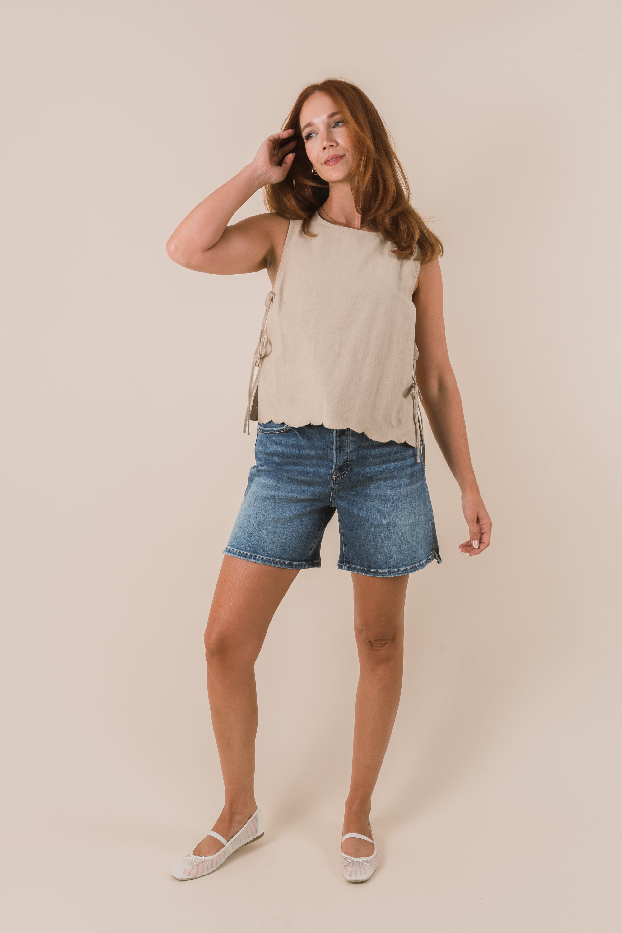 Woman wearing a beige sleeveless top and denim shorts on a beige background