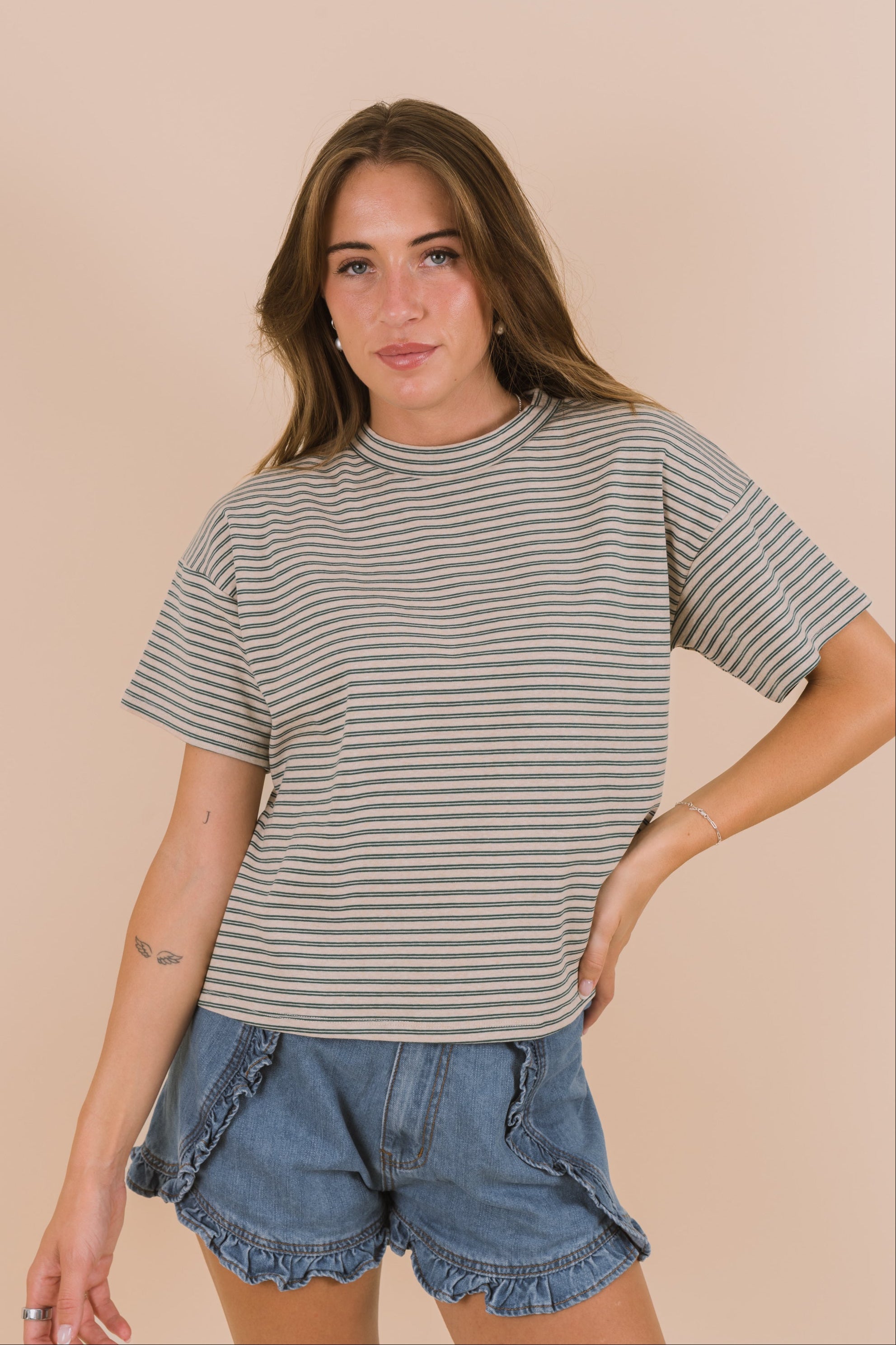 Woman wearing a striped t-shirt and denim shorts against a beige background