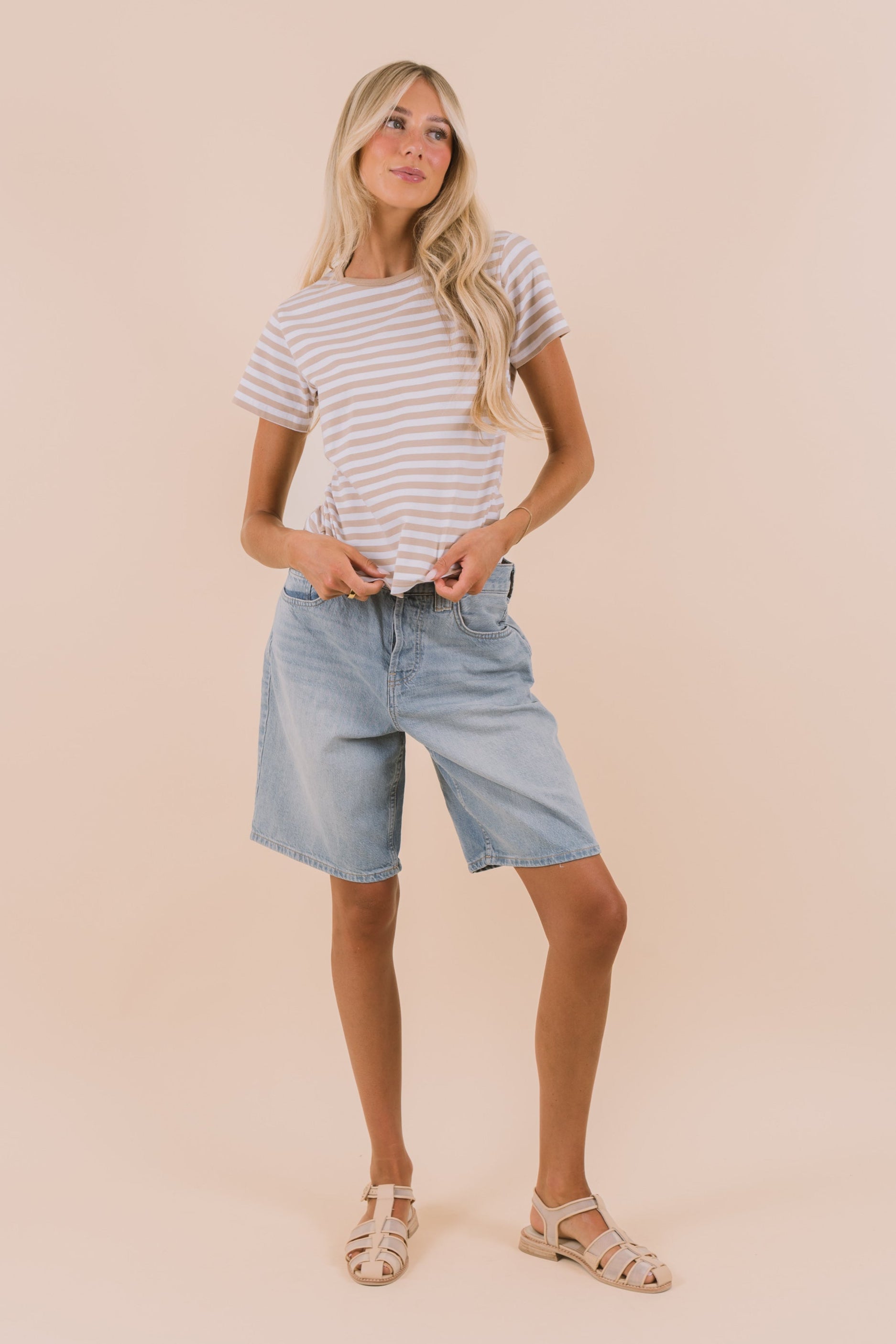 Woman wearing a striped shirt and light blue shorts against a beige background