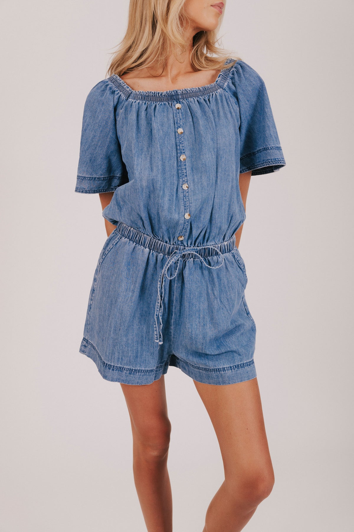 blue denim romper with buttons down the front and a tie at the waist