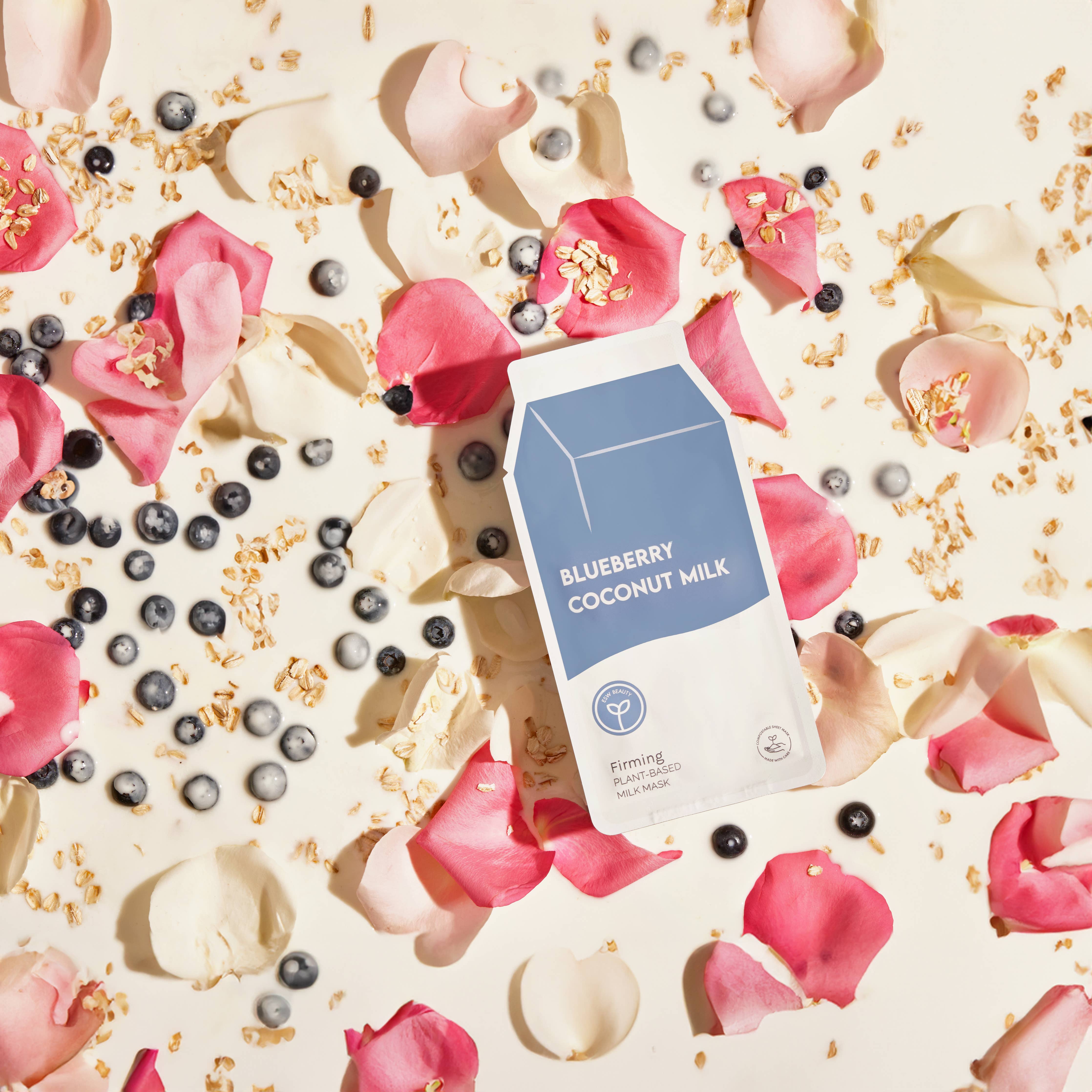A sheet mask package labeled 'Blueberry Coconut Milk' firming plant-based milk, presented on a background with blueberries, petals, and oats.