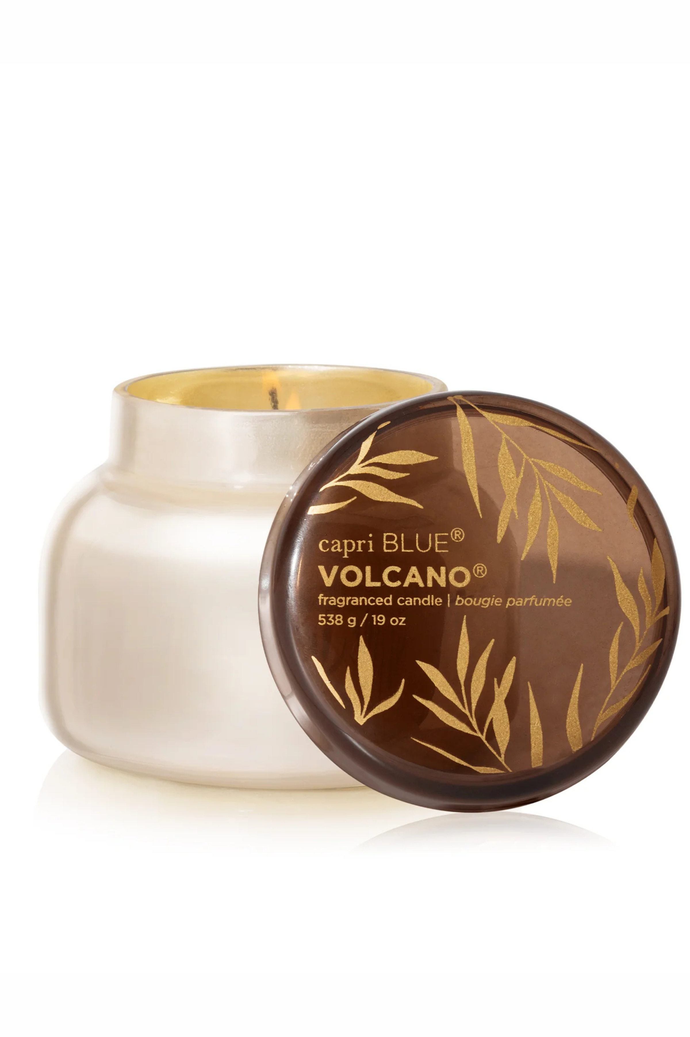 Pearlescent white glass candle with brown class lid with gold accents in volcano by capri blue.