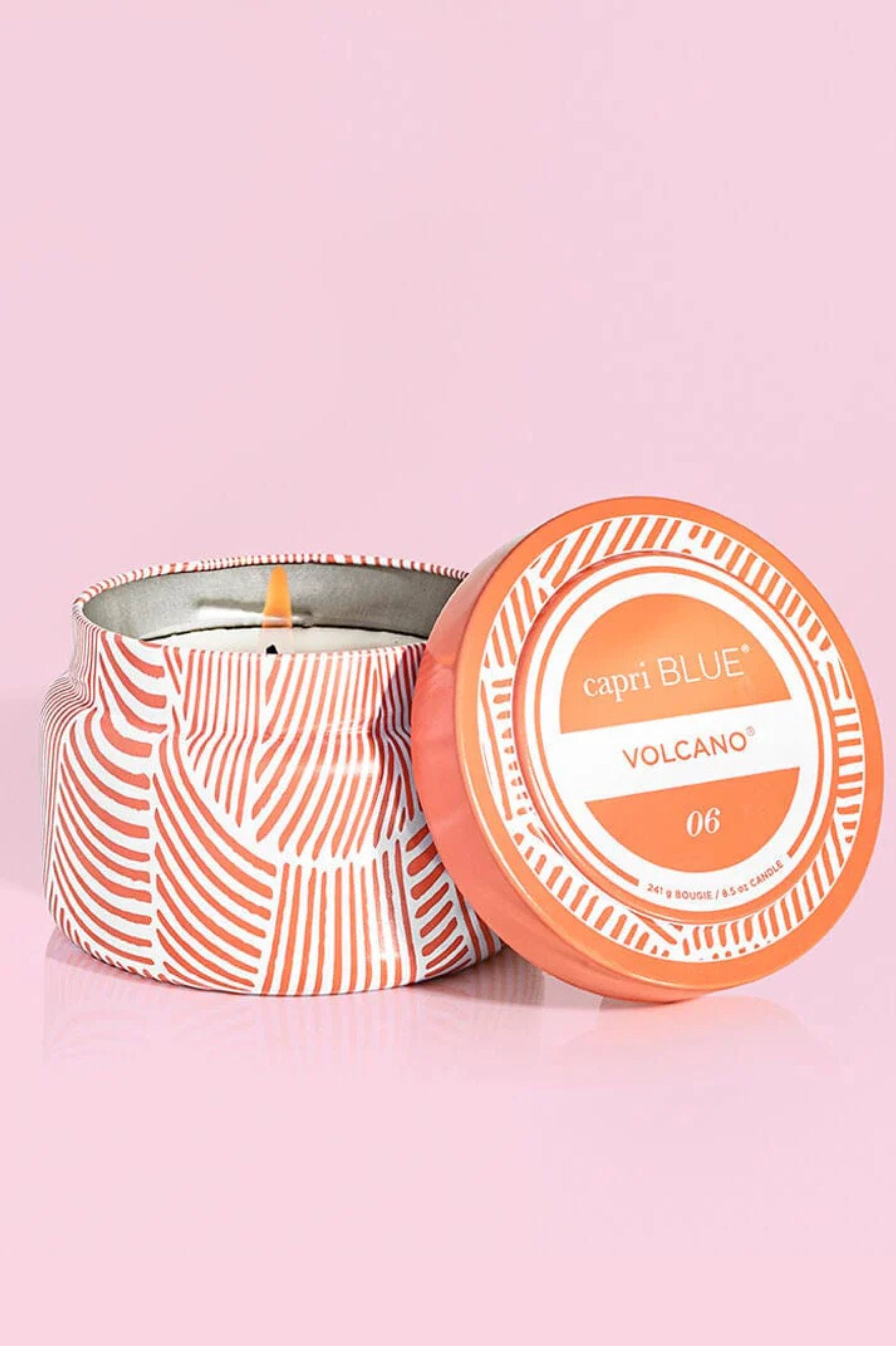 Candle in a decorative tin with a matching lid on a pink background