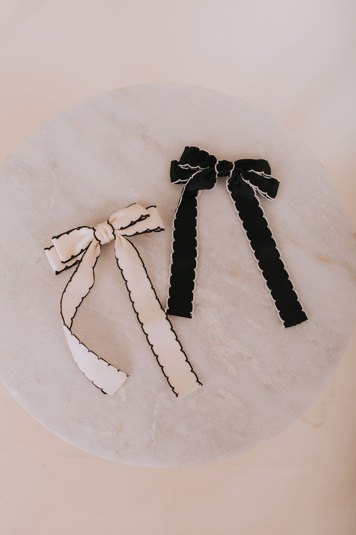 Two hair bows, one white and one black, on a marble surface.