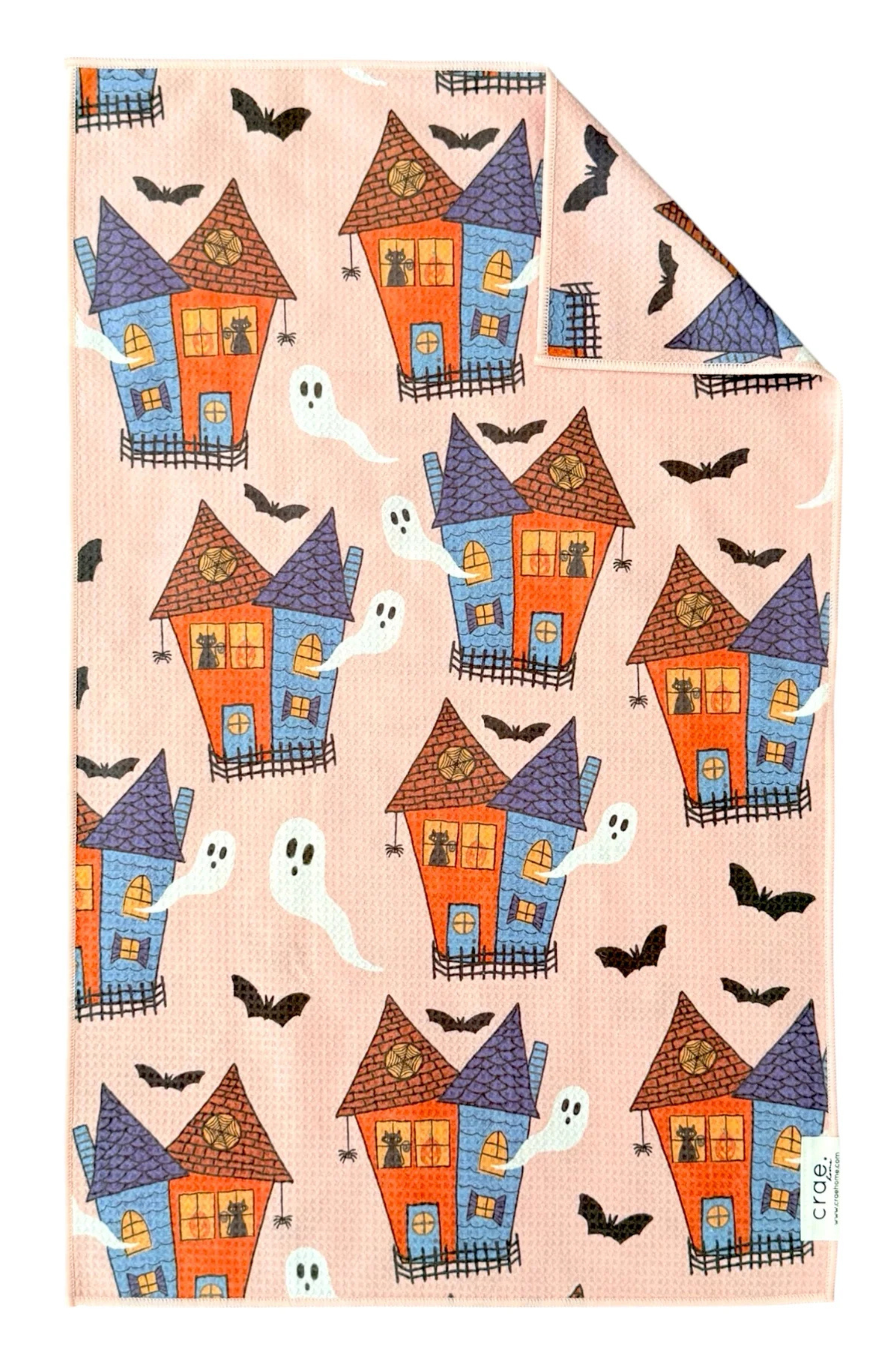 Patterned microfiber towel with Halloween-themed houses, ghosts, and bats on a peach background.