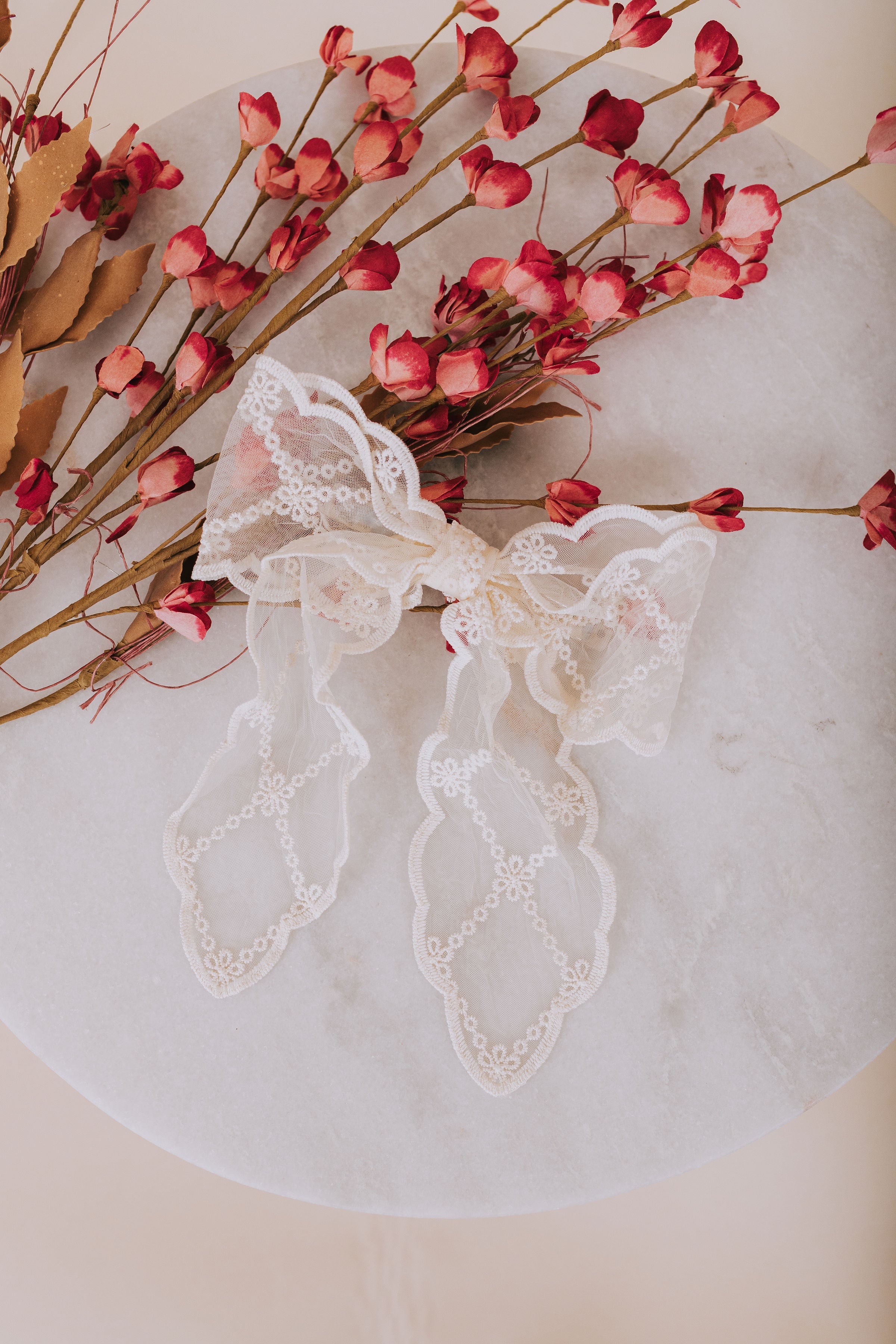 Lace hair bow with scalloped trim and embroidered flower pattern on a french clip 