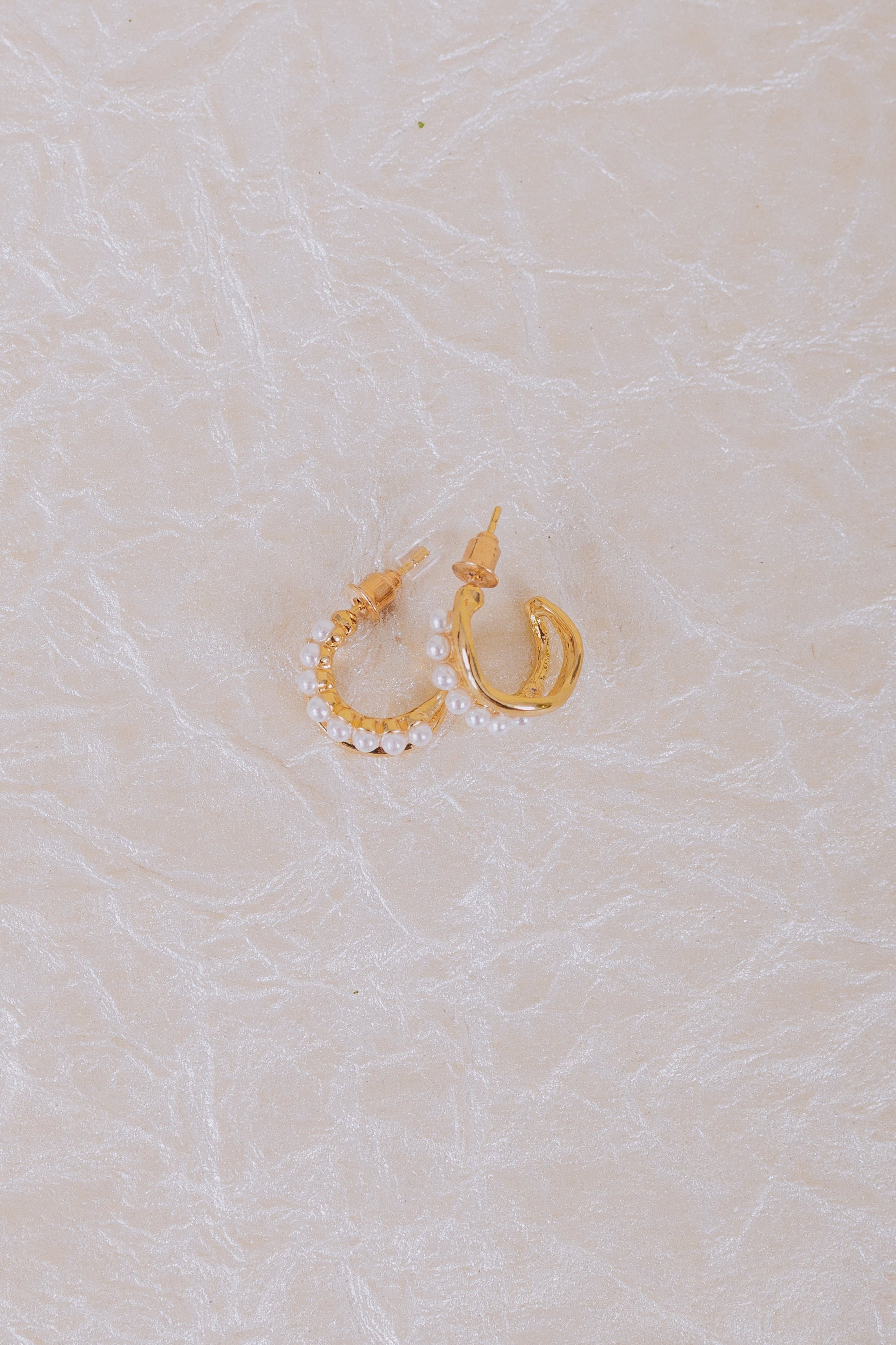 Gold hoop earrings with pearl details on a textured beige surface