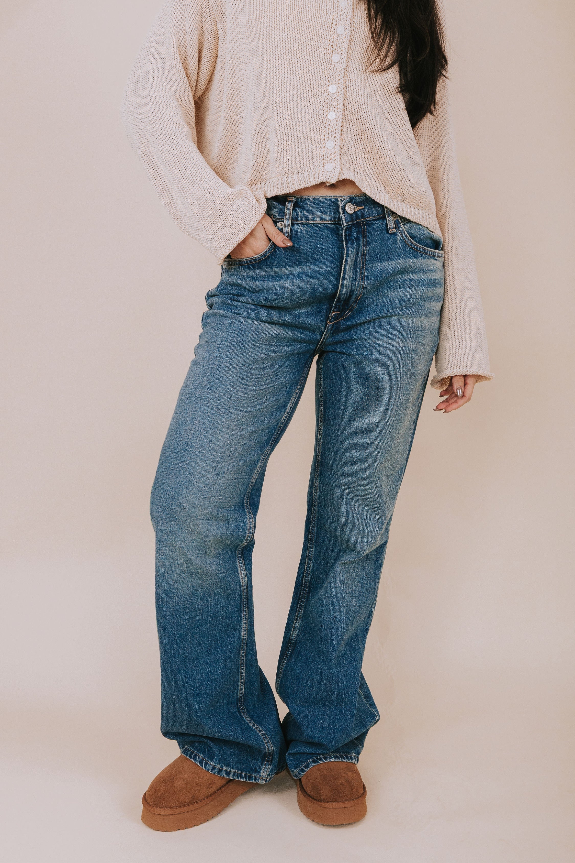 Person wearing blue jeans and a beige cardigan on a plain background