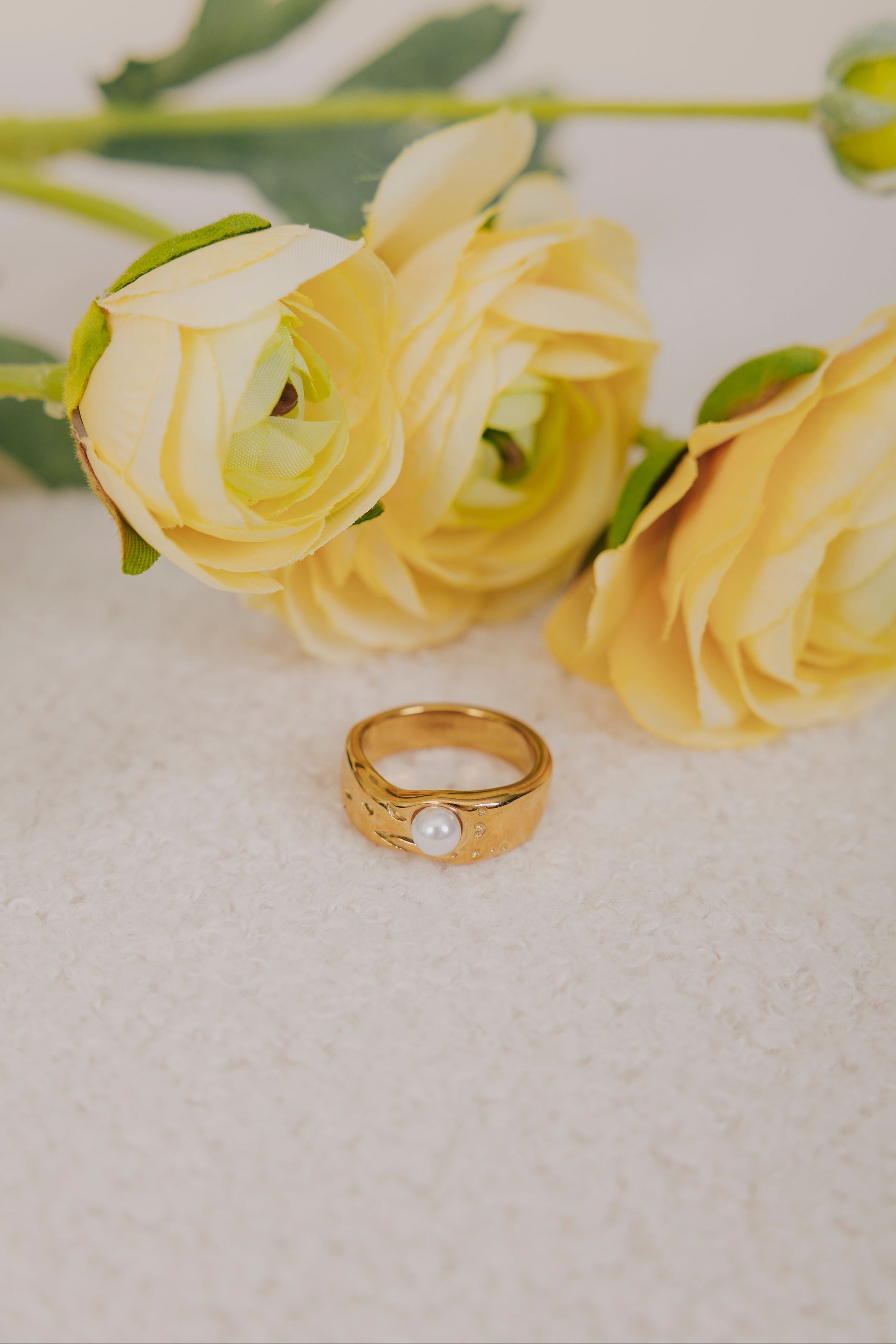 Gold ring with a pearl on a white surface with yellow flowers in the background