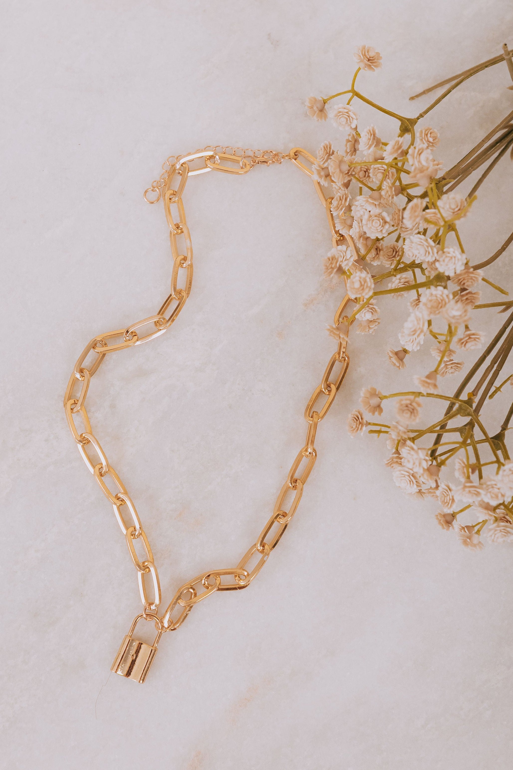 Gold chain necklace with a lock pendant on a light background with small flowers.