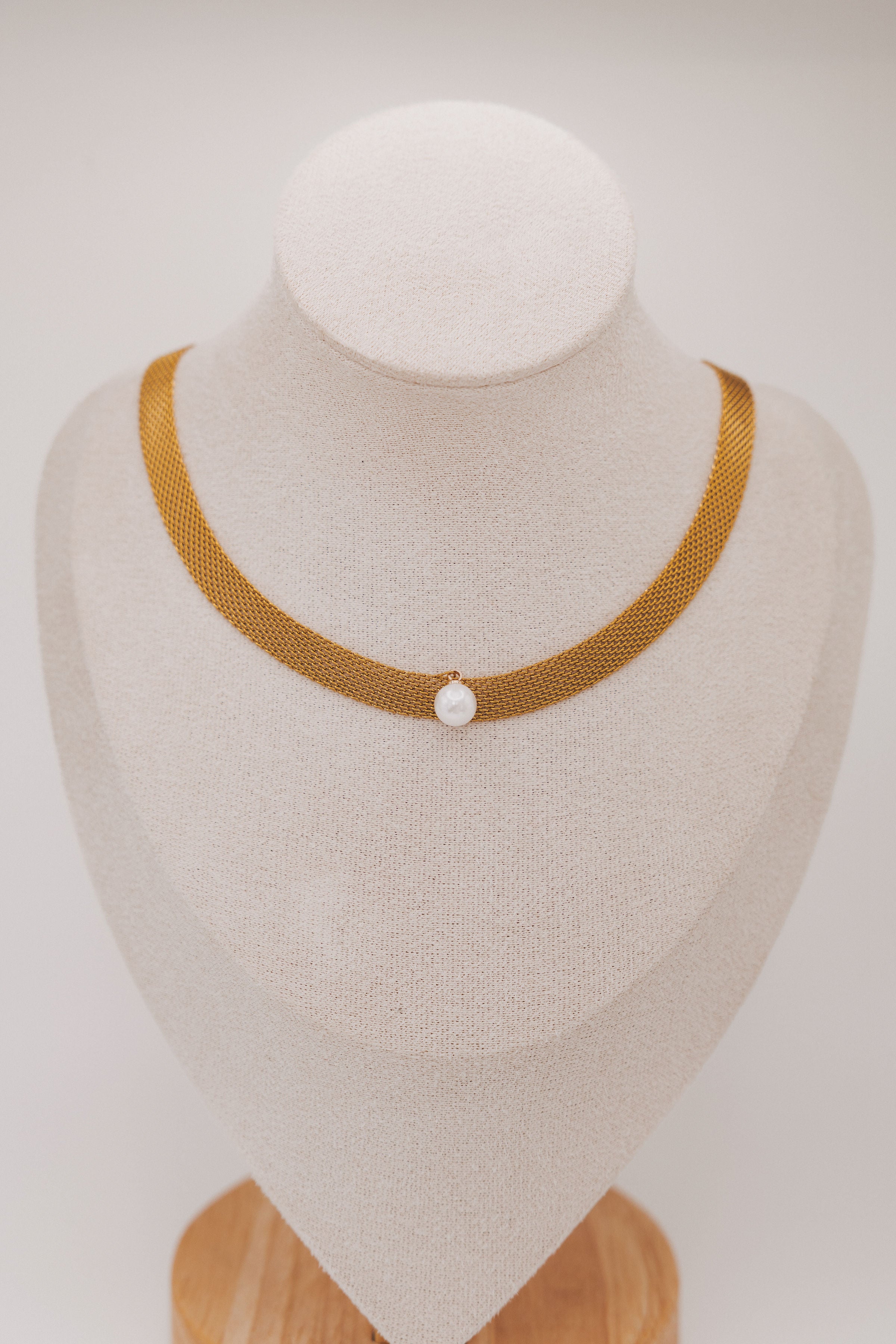 Brown mesh necklace with a pearl on a mannequin bust against a white background