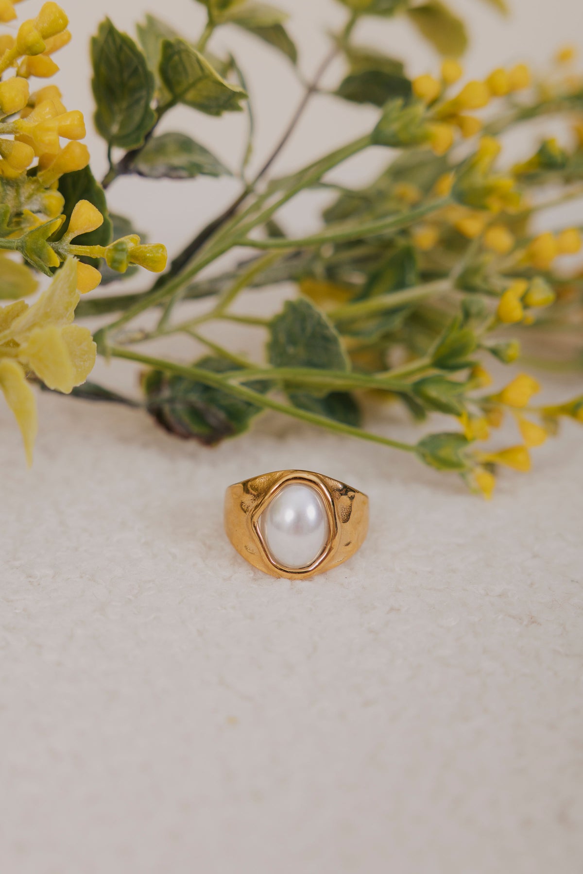 Gold ring with a pearl on a light background with yellow flowers