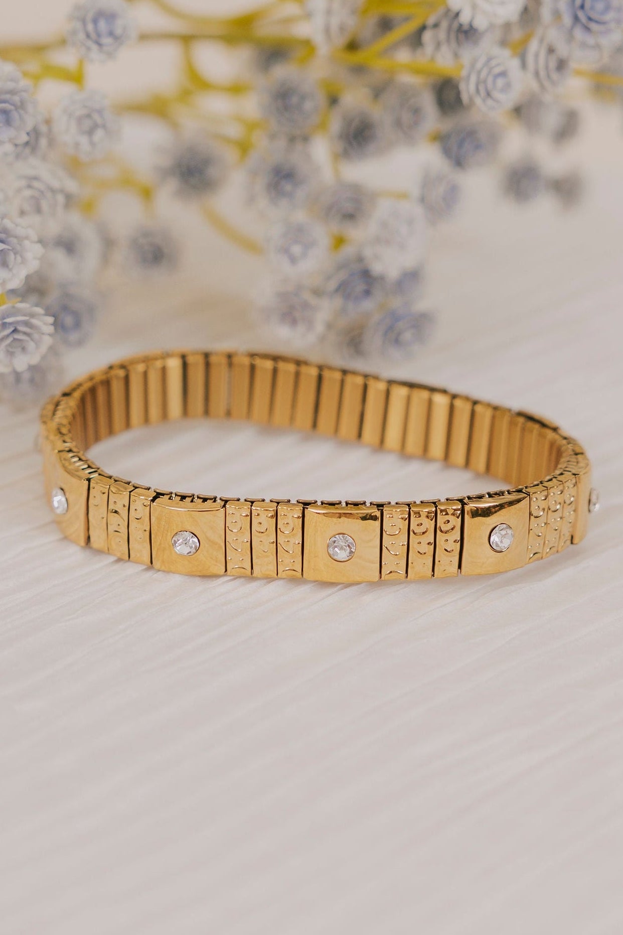 Gold bracelet with small diamonds on a light surface with flowers in the background