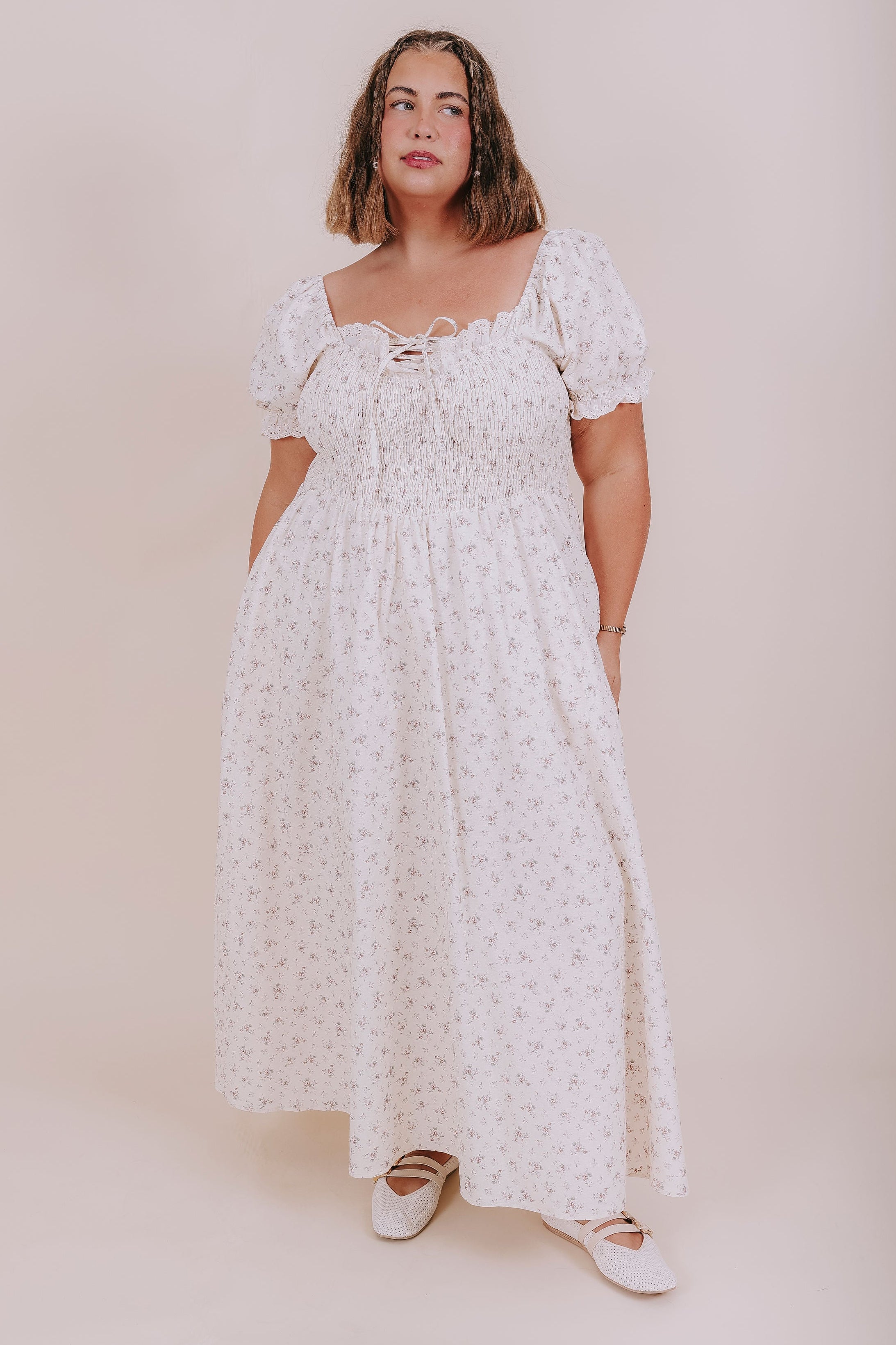 Woman wearing a white floral dress against a plain background