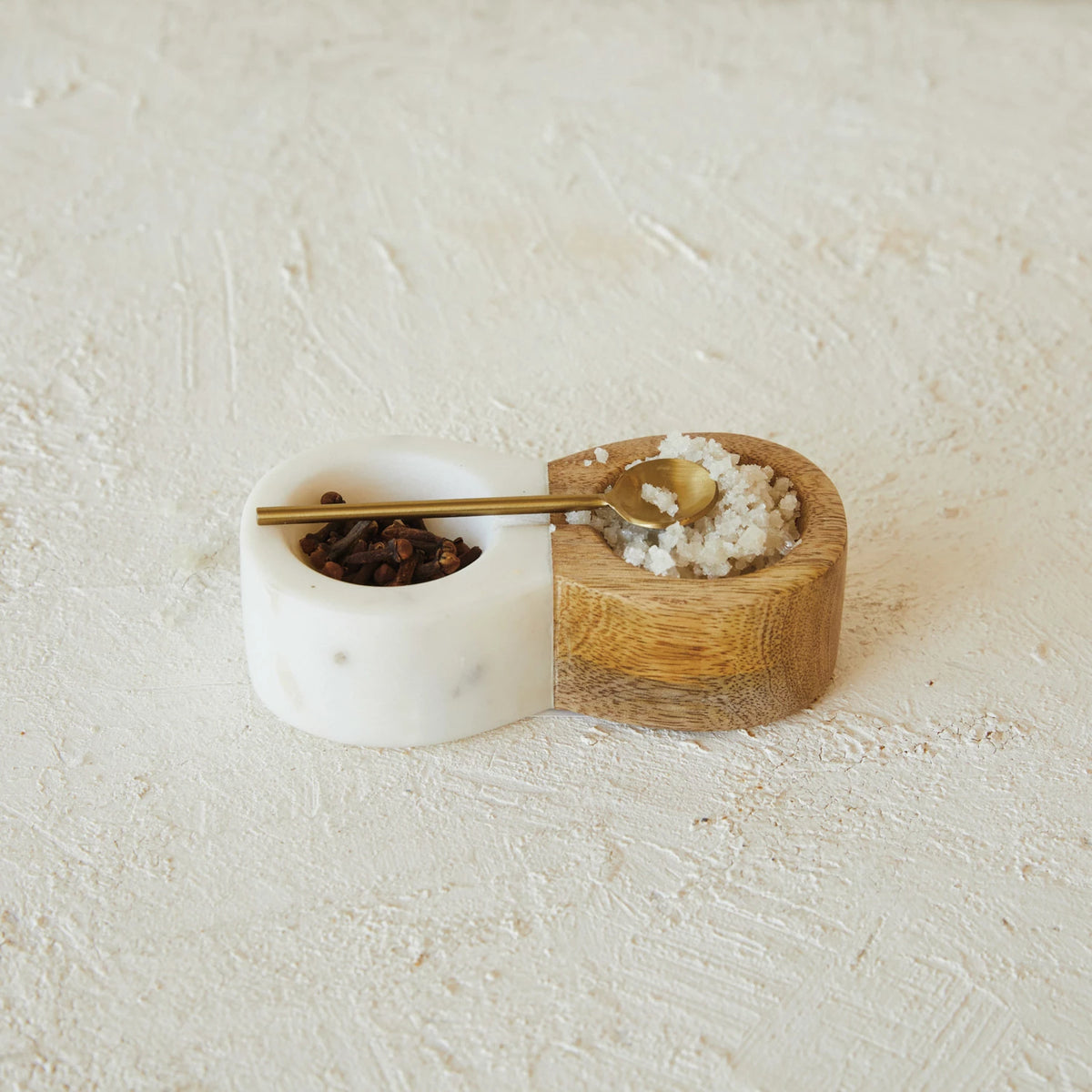 Marble container with gold spoon, wooden holder with salt, on textured beige surface