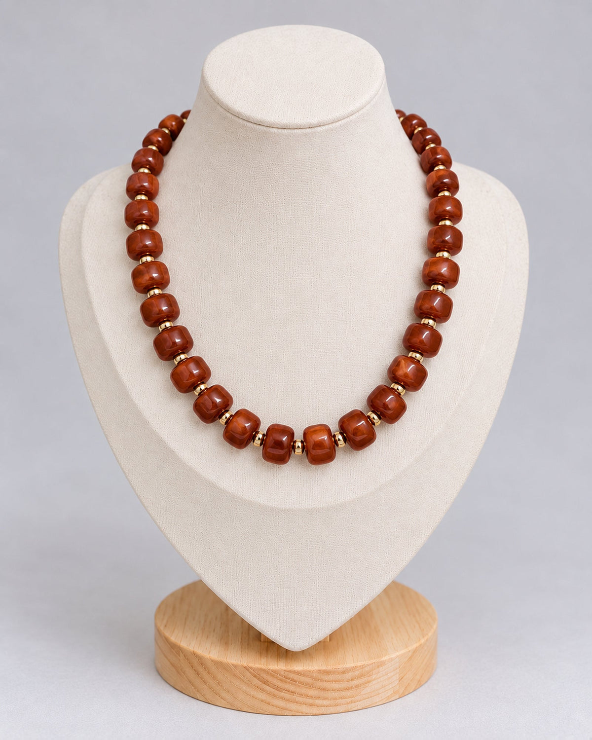 Reddish-brown marbled beaded necklace with gold-tone spacers on an ivory jewelry bust