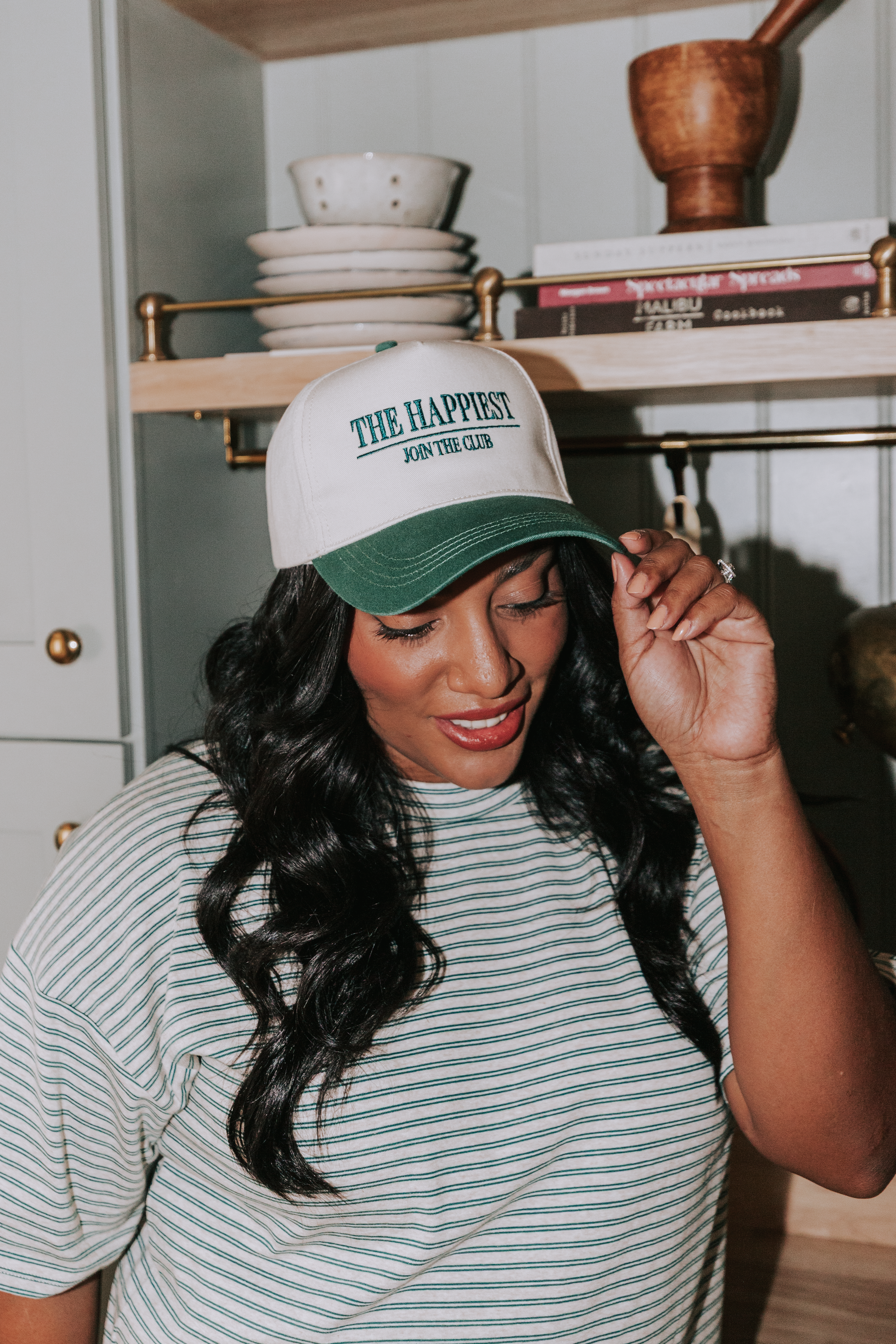 Woman wearing a cap with 'The Happiest' text in a kitchen setting