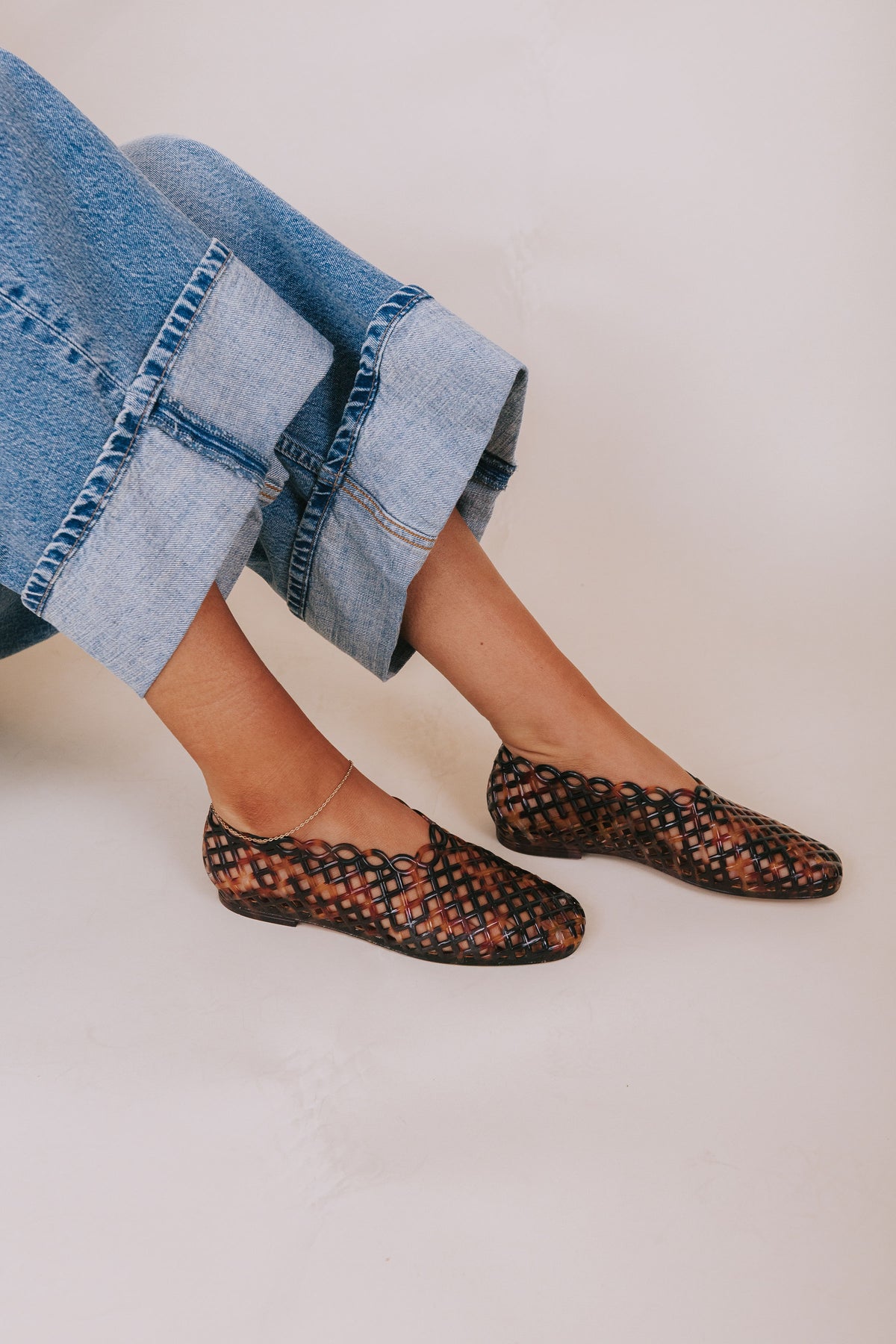 Person wearing leopard print flats and rolled-up jeans on a plain background