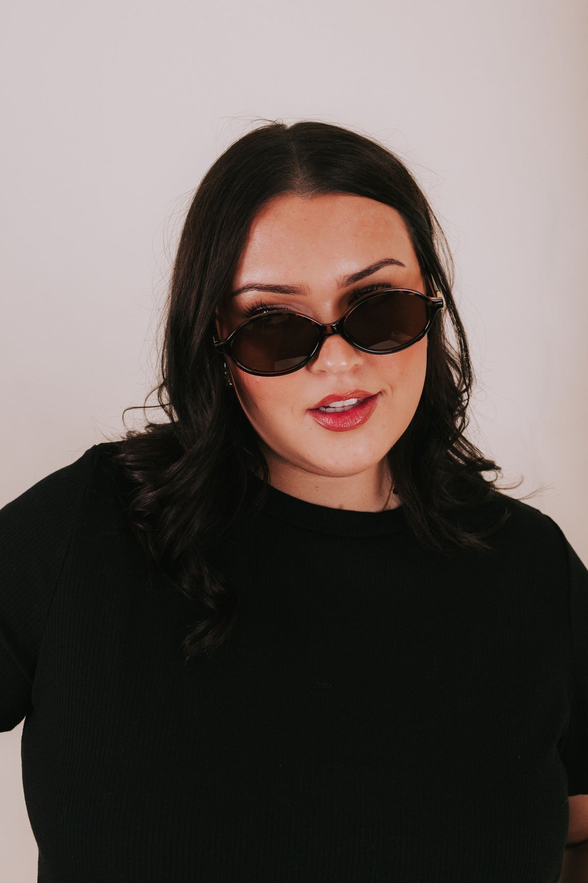 Woman wearing tortoise oval sunglasses with brown lenses staring at the camera 