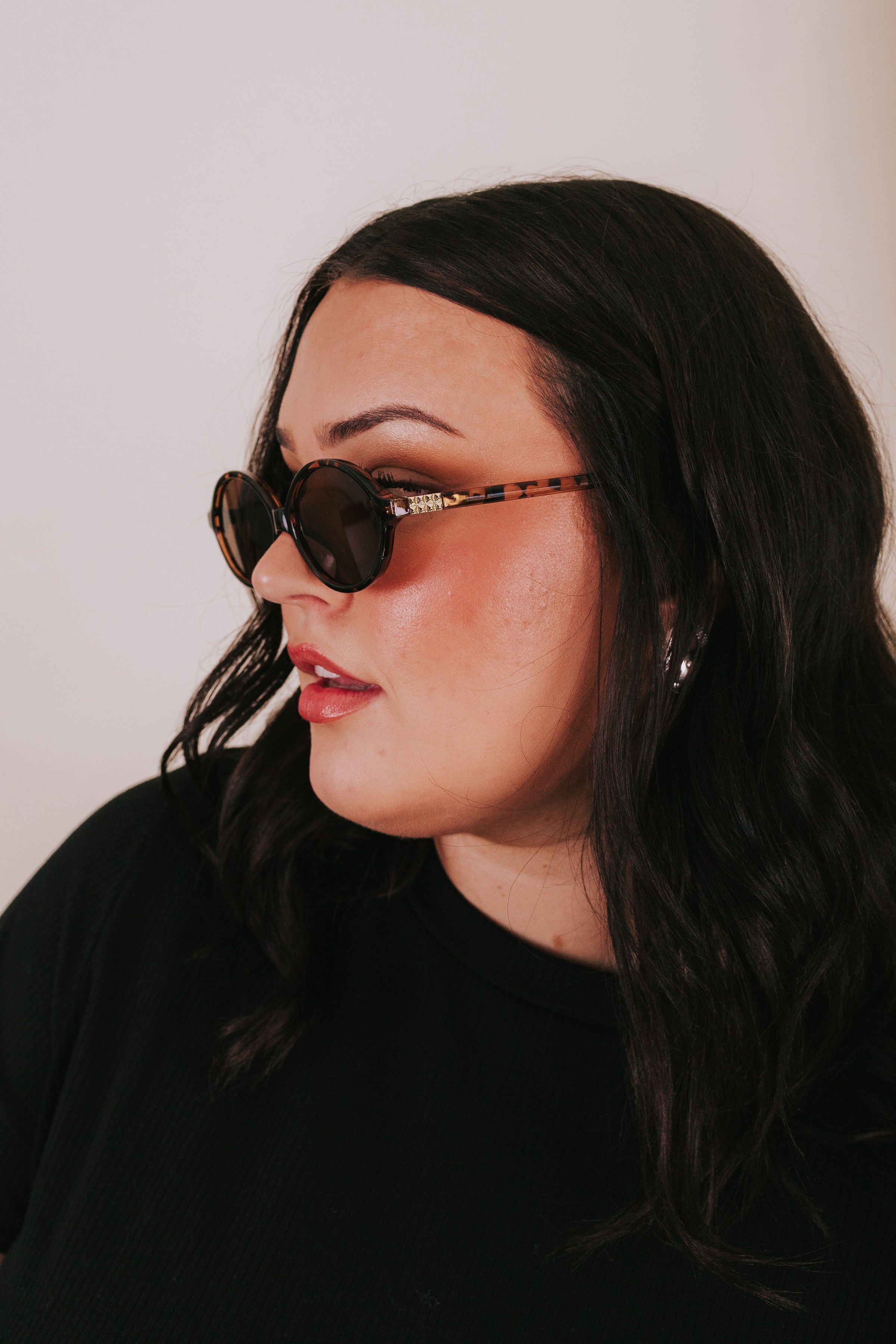 Woman wearing oval tortoise sunglasses with gold stud detailing on the side 