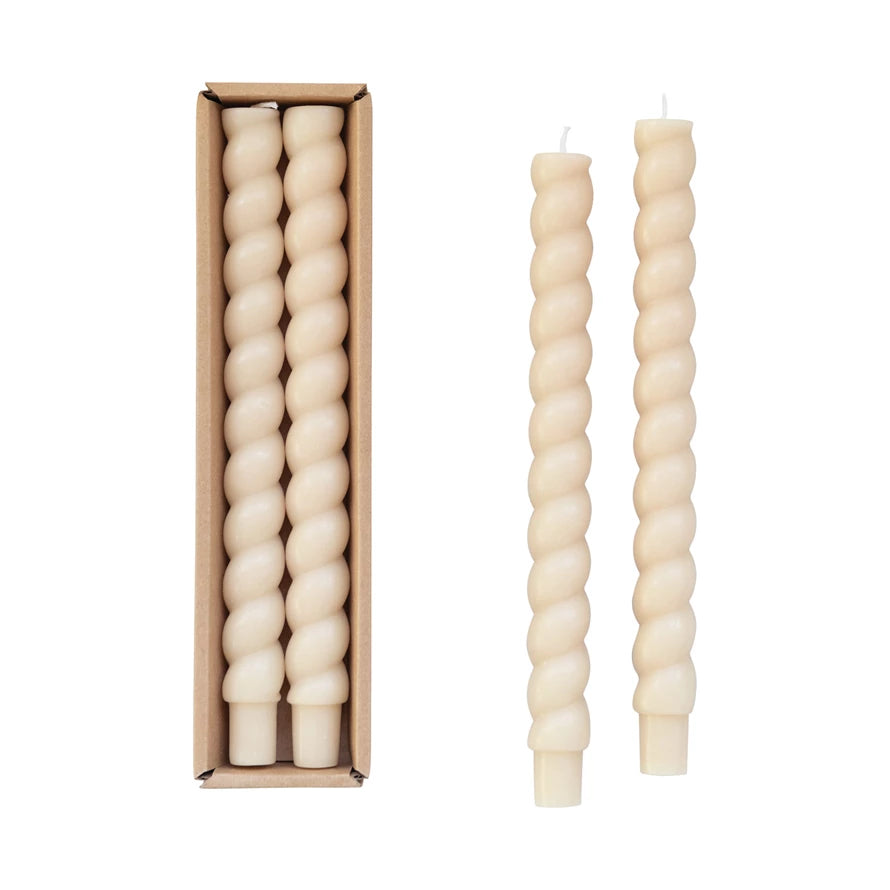A set of two beige, twisted taper candles displayed both outside and inside of a cardboard box.