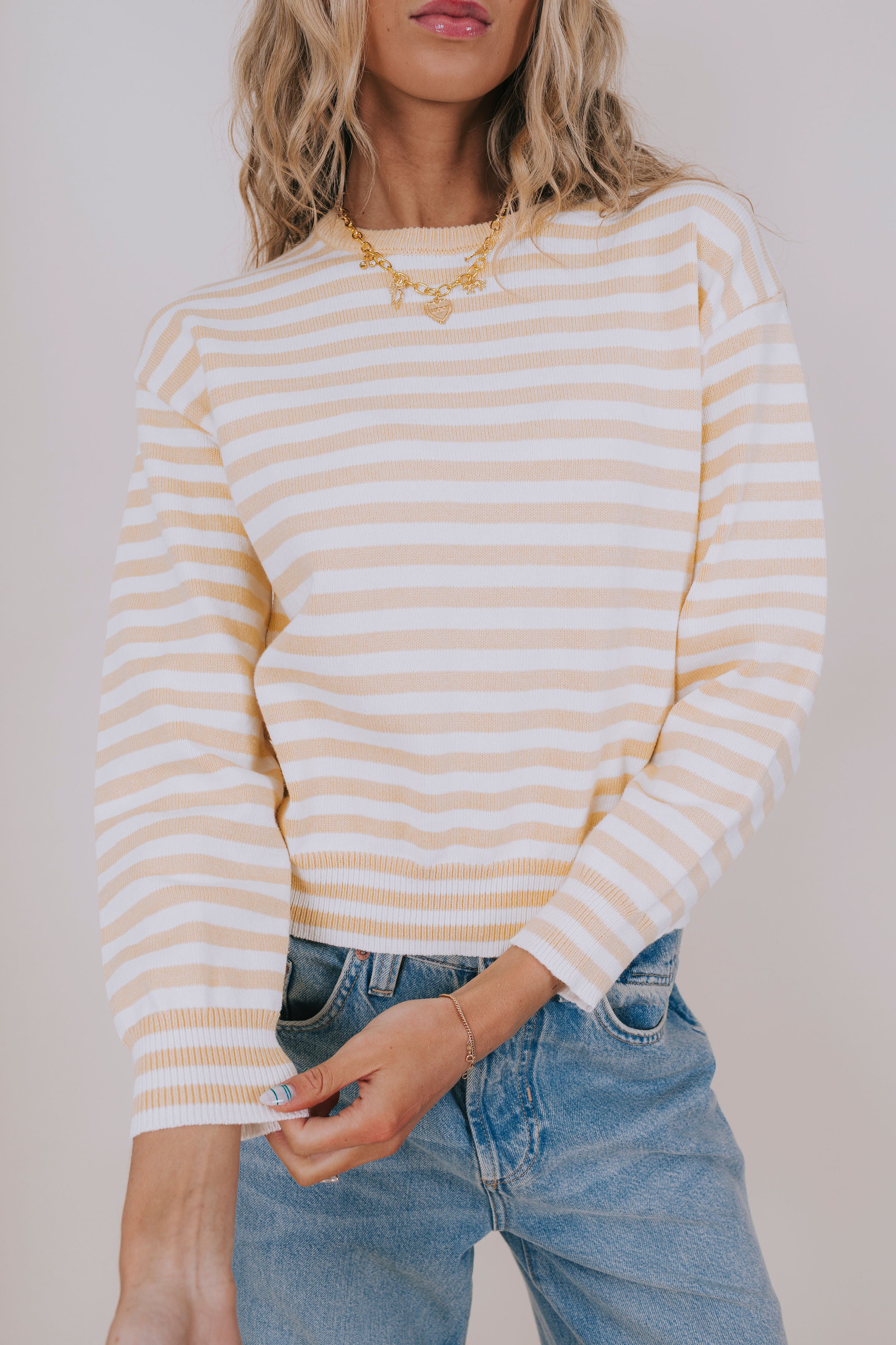 Woman wearing a yellow and white striped sweater with blue jeans against a plain background