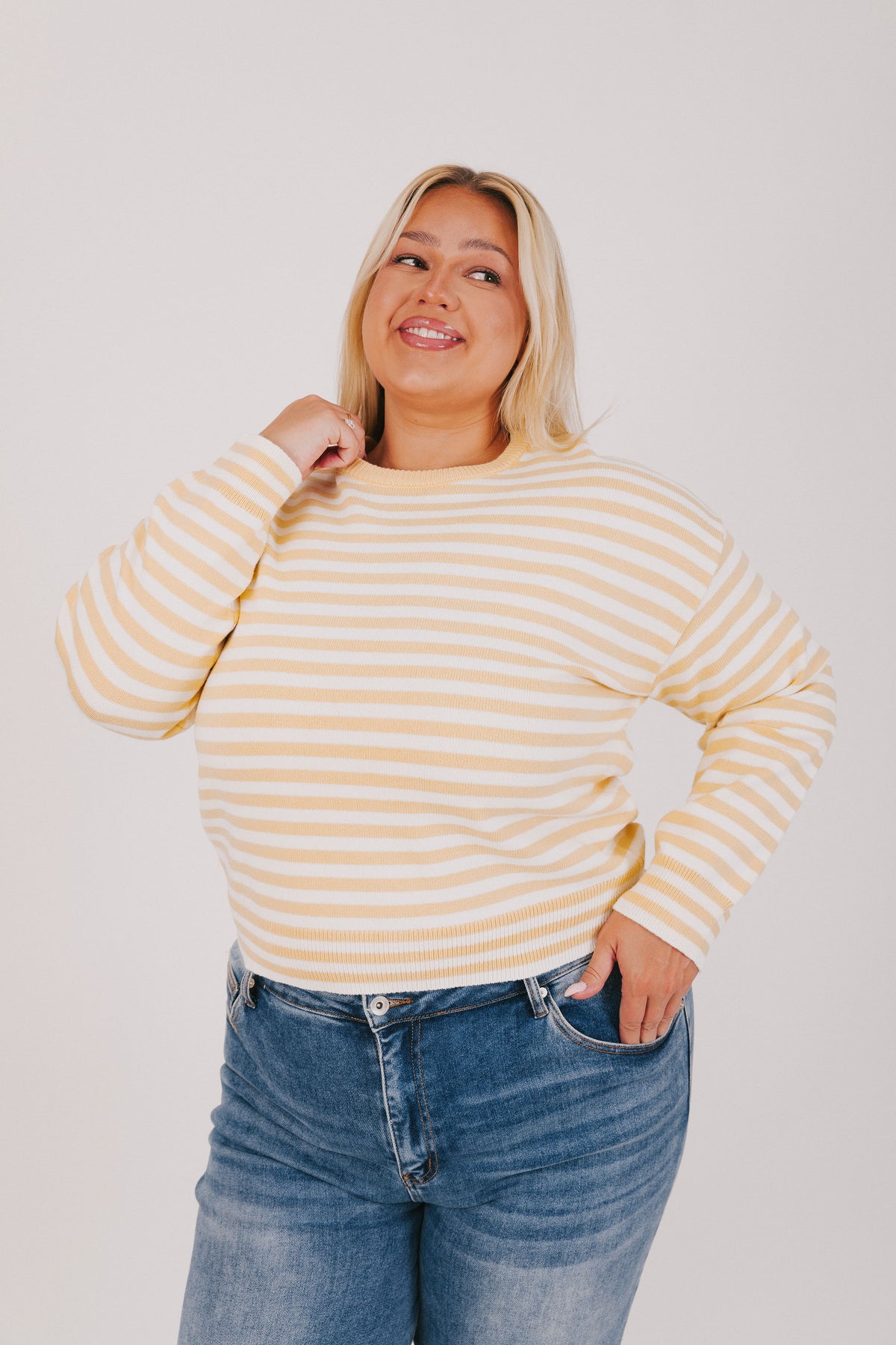 Woman wearing a striped sweater and blue jeans against a plain background