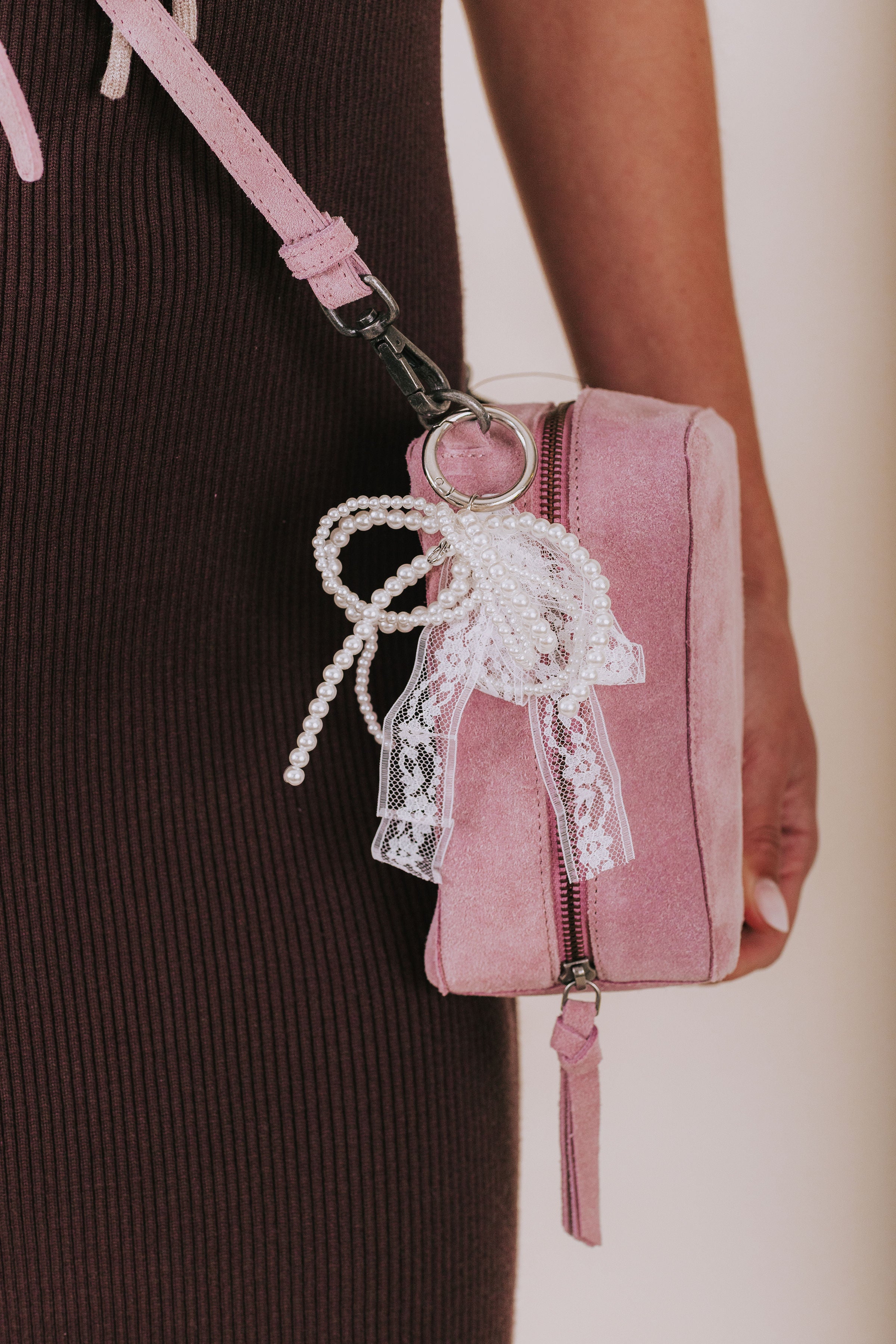 Pink handbag with lace detail held by a person wearing a dark ribbed sweater.