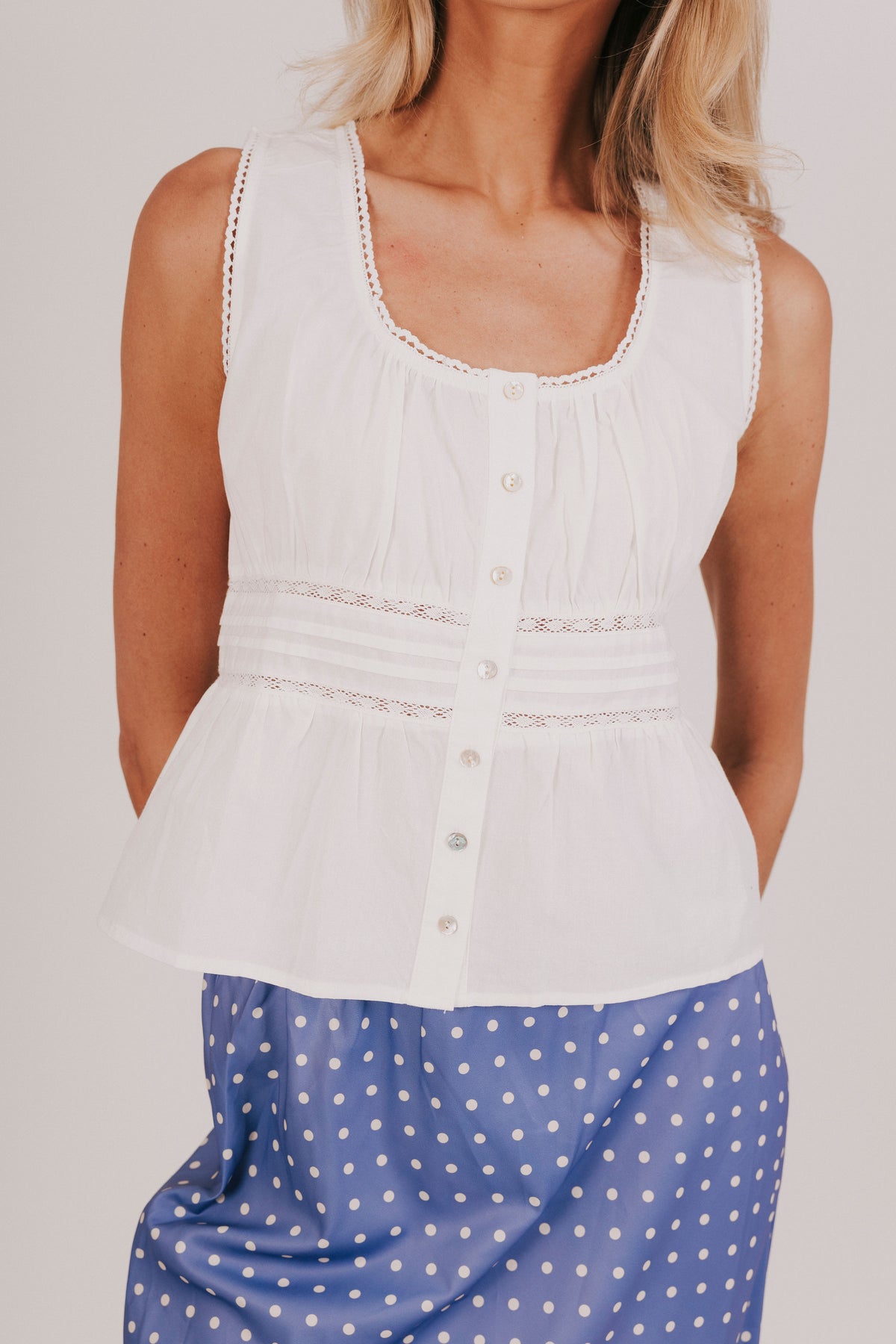 White sleeveless blouse with gathered lace, and pin-tucked details. 